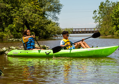 One boy and one girl paddling in a green kayak